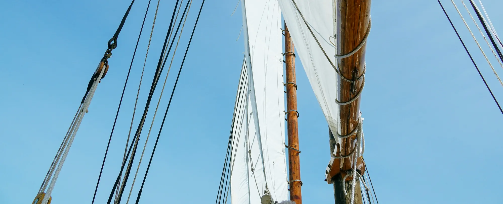 Close-up view of sailboat masts with sails unfurled against a clear blue sky.