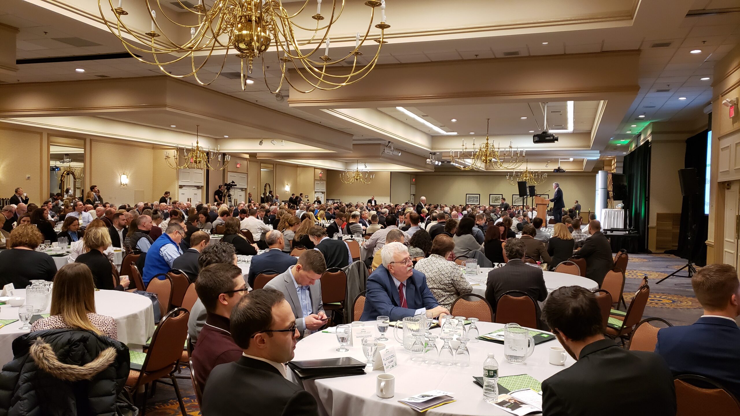 Conference guests in ballroom as presenter speaks.